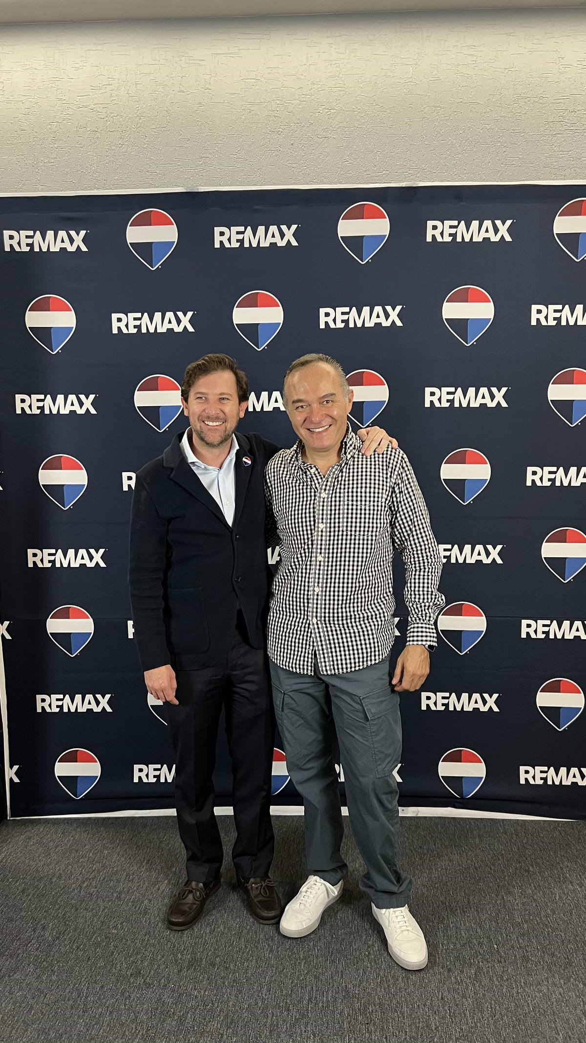 David Murphy junto a un directivo de RE/MAX frente al mural de logotipos de la marca.